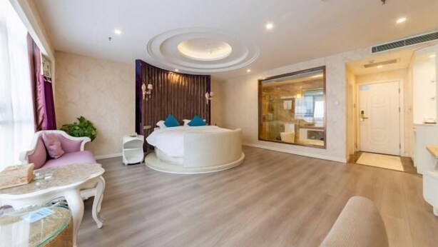 A modern hotel room with a round jacuzzi, a glass-enclosed shower, a pink sofa, and a small table. - Lanzuan Hotel (Ankang)