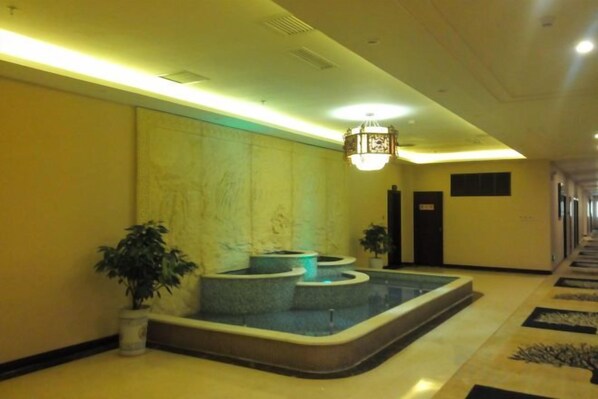 Un vestíbulo de hotel con una recepción, una zona de estar con una fuente y un pasillo con puertas.