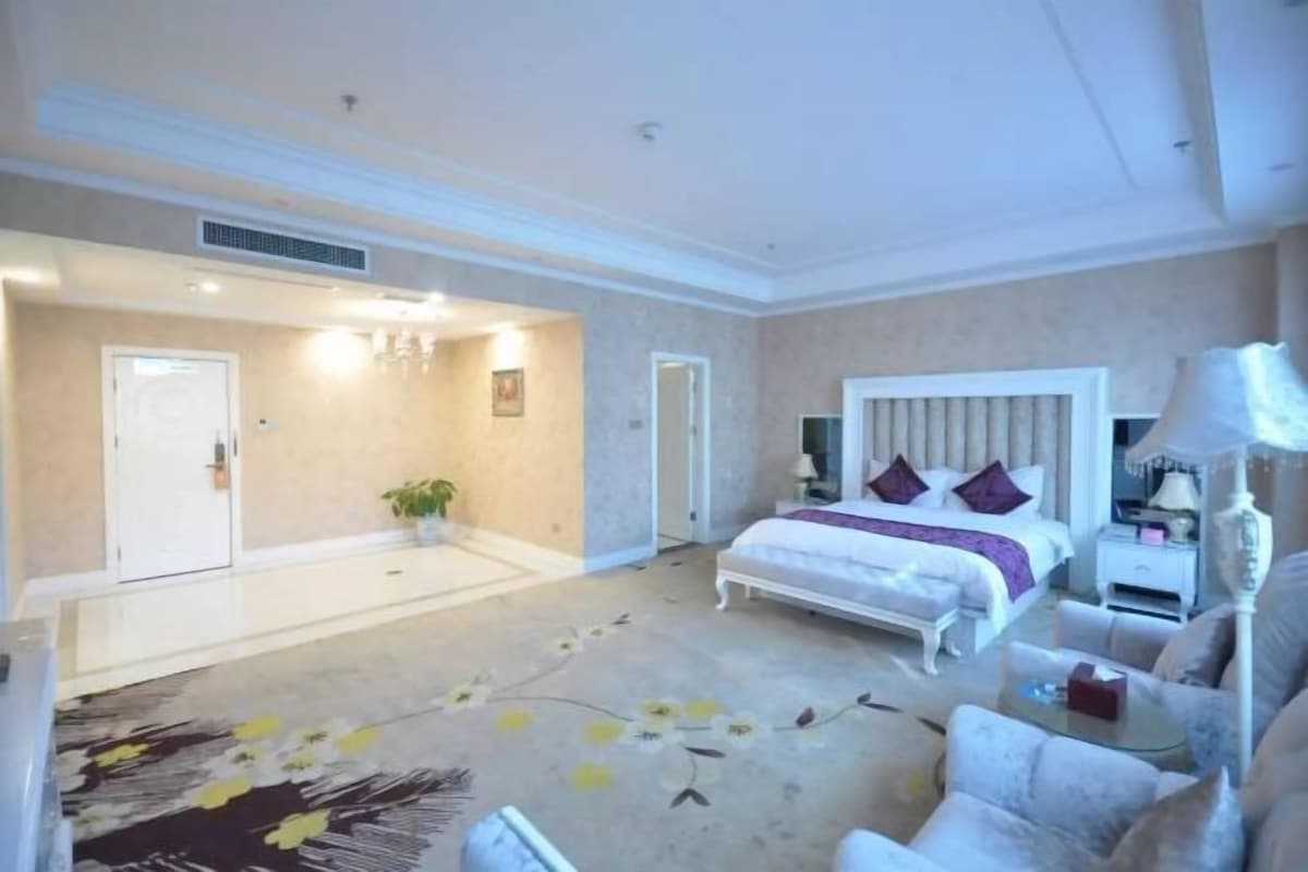 A hotel room with a bed, bedside table, lamp, and a carpet with a floral pattern.