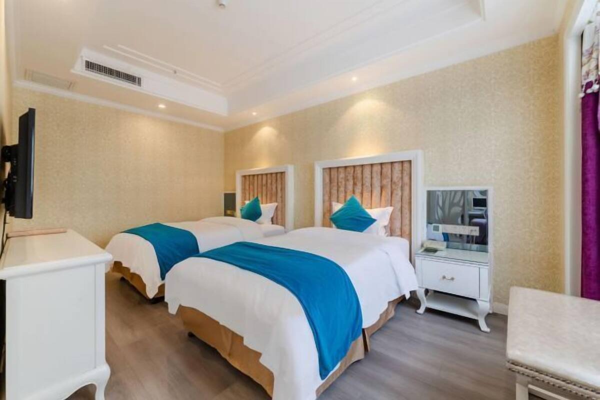 A hotel room with two beds, a TV, a vanity with a mirror, and a bedside table.
