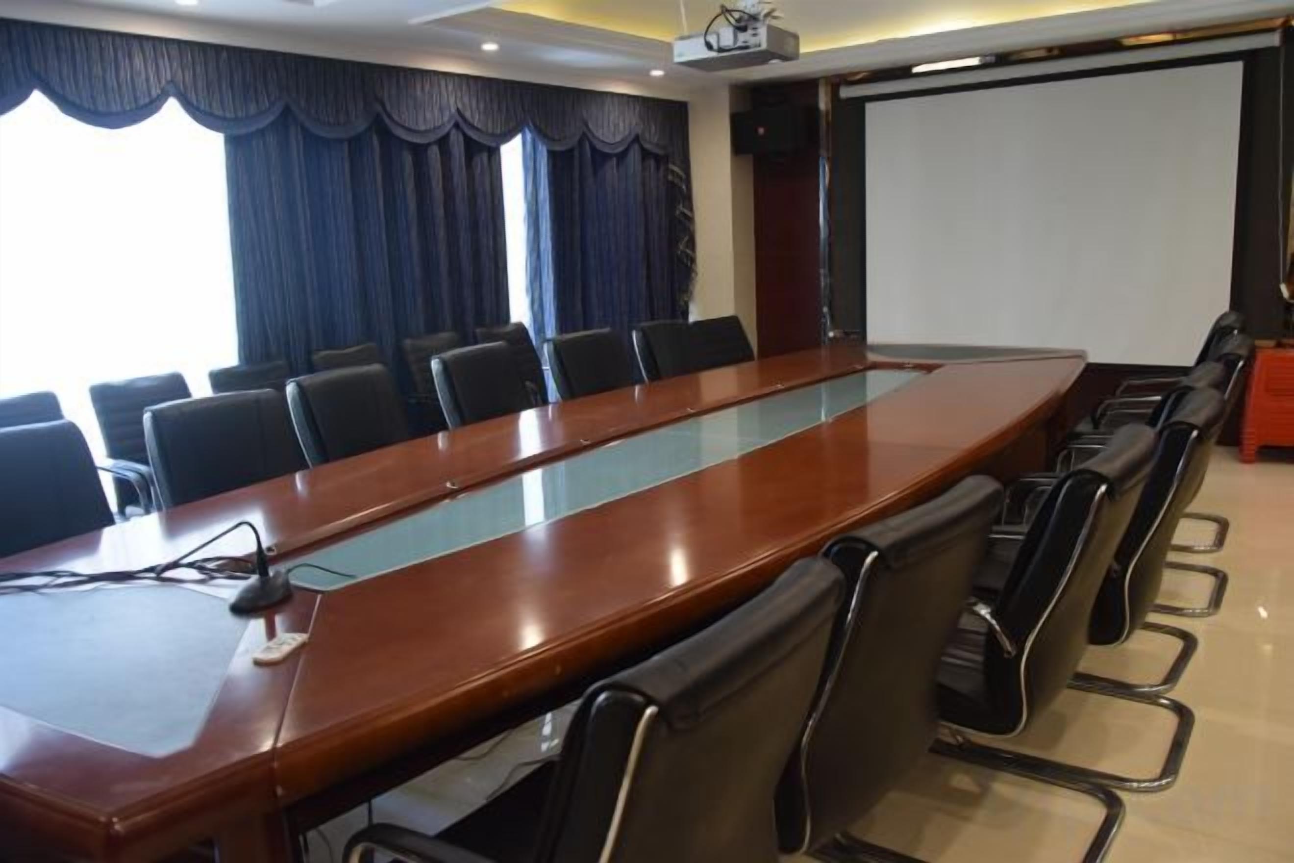 A conference room with a long table, chairs, a projector, and a screen.
