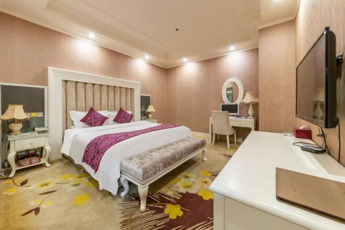 A hotel room with a bed, bedside table, chair, desk, and a television.