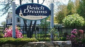 A sign for Beach Dreams Cottages with a stone wall and pink flowers in front. - Sweet Beach Dreams (Wells)