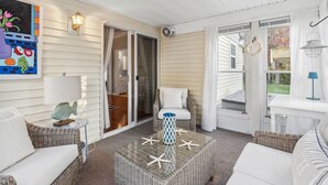 A covered patio with wicker furniture, a glass coffee table with starfish, and a painting on the wall. - Sweet Beach Dreams (Wells)