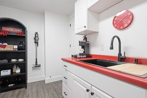 A modern kitchen with a red countertop, white cabinets, a black faucet, and a red clock on the wall. - Assembly Hall Hideaway  - Walk to Stadiums! (Bloomington)