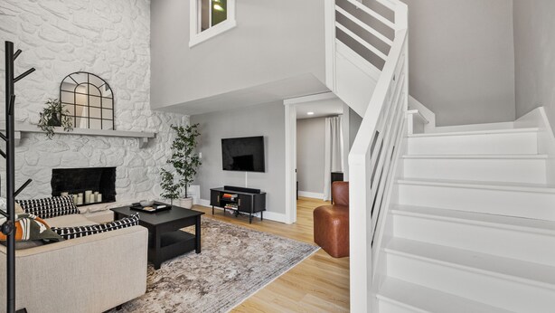 A modern living room with a stone wall, a fireplace, a flat-screen TV, and a staircase. - Hoosier HQ: Sleek 3-Bed Near IU (Bloomington)