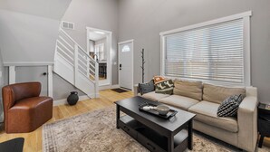 A modern living room with a staircase, a sofa, a coffee table, and a leather chair. - Hoosier HQ: Sleek 3-Bed Near IU (Bloomington)