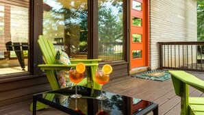 A wooden deck with two green chairs and a glass table, two drinks with orange slices, and a red door with the number 1316.