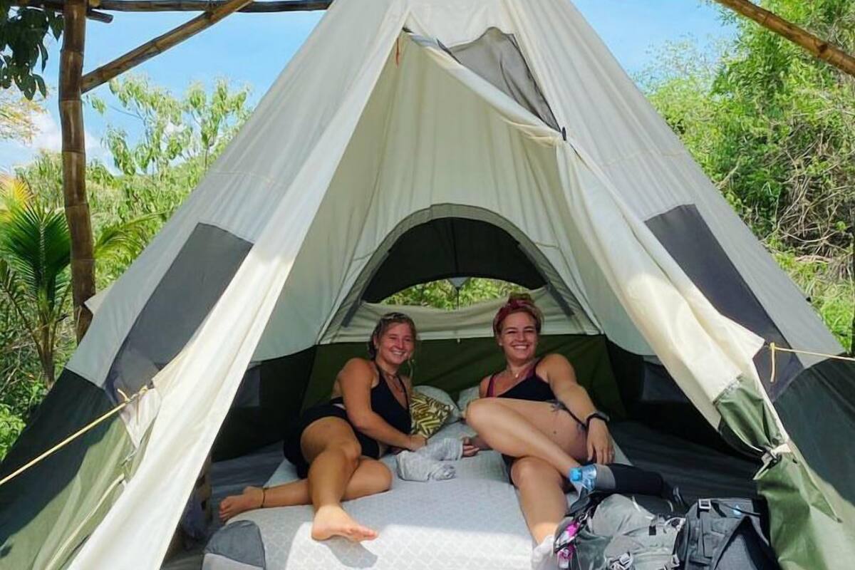A tent with a simple, open design, two people sitting inside, and a backpack on the ground.