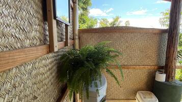 A bathroom with a woven wall, a white toilet, a potted plant, and a trash bin.