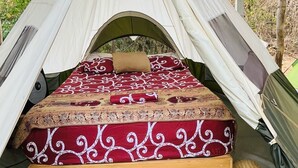 Een tent met een bed erin, met een beddegoed en kussens met een patroon.