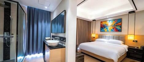 Une chambre d’hôtel moderne dotée d’une douche à parois de verre, d’un grand lit, d’une table de chevet et d’un tableau au mur.