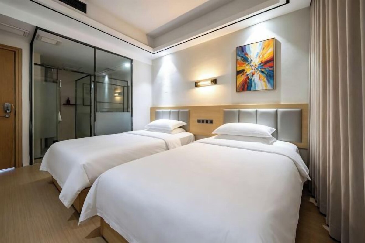 Une chambre d’hôtel avec deux lits, une douche en verre et un tableau au mur.