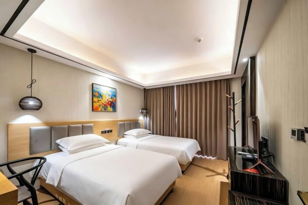 Une chambre d’hôtel avec deux lits, un bureau, une chaise, une télévision et un tableau au mur.