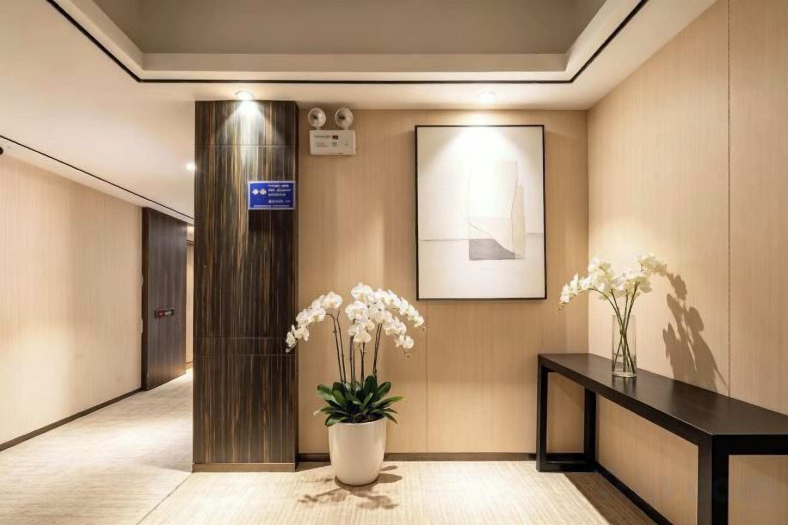 A hotel lobby with a reception desk, a potted plant, a framed artwork, and a vertical sign.