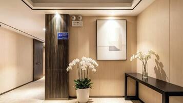 A hotel lobby with a reception desk, a potted plant, a framed artwork, and a vertical sign.