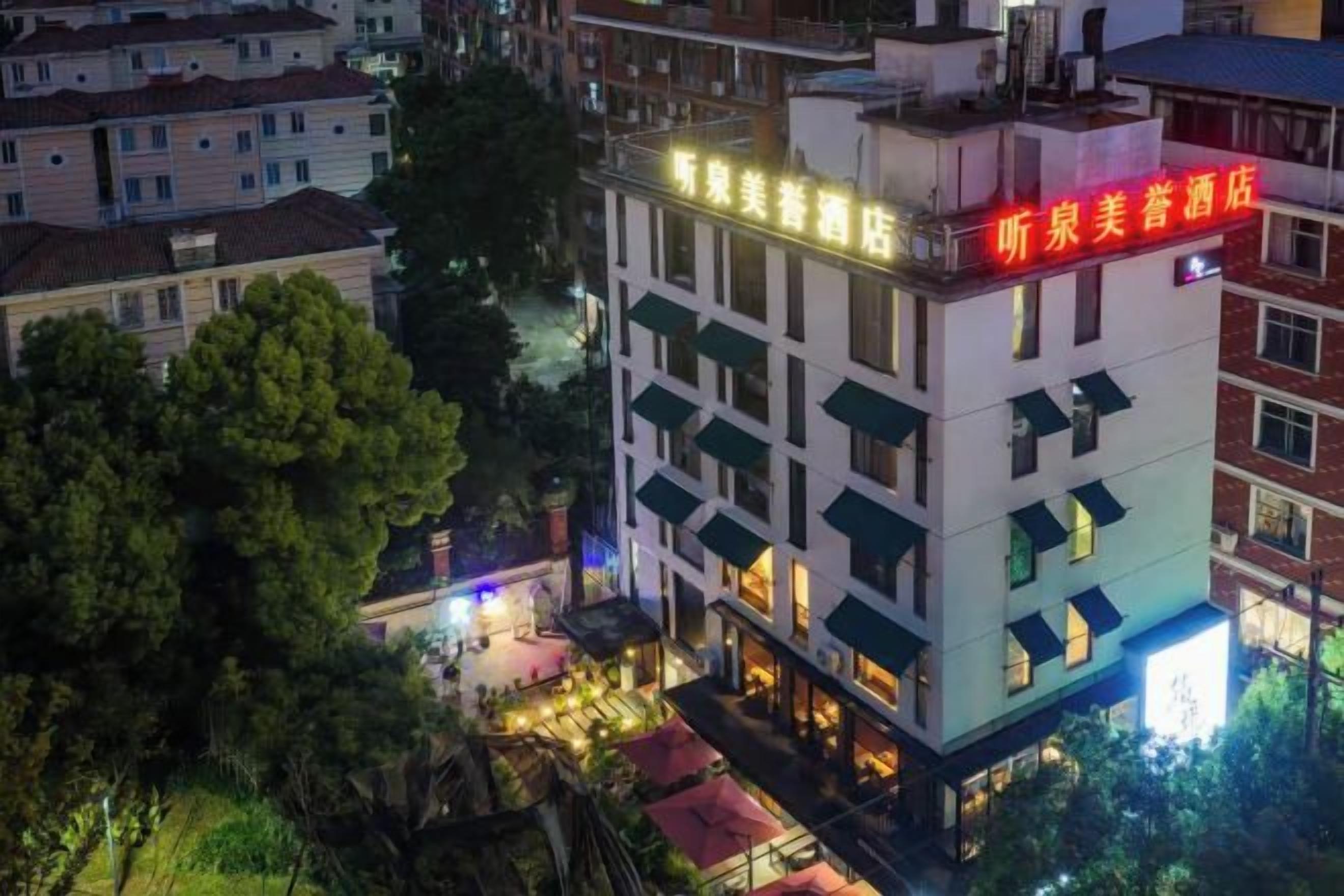 A multi-story hotel with a prominent red sign on the top floor, surrounded by other buildings and trees.
