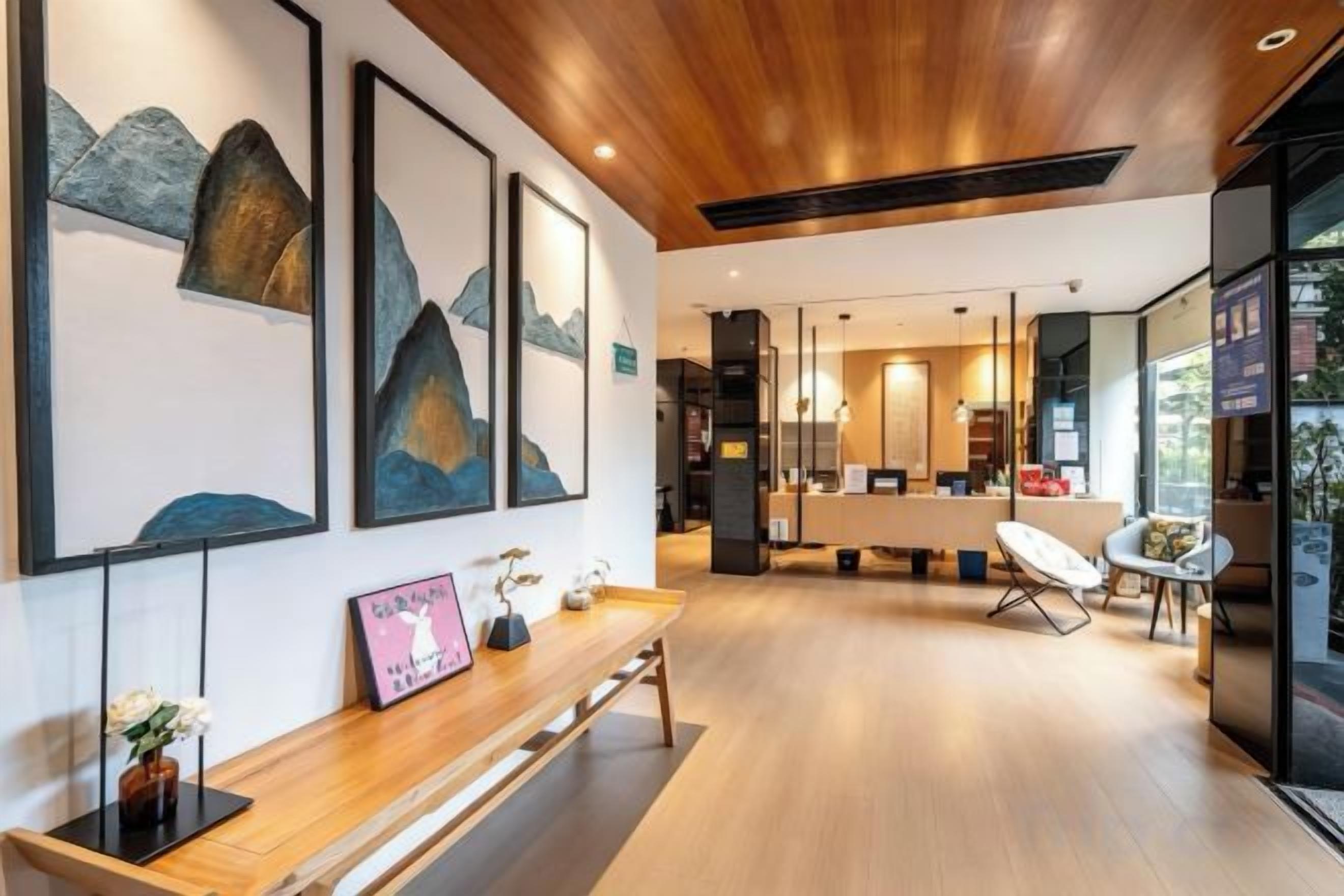 A modern interior with a wooden ceiling, a reception desk, framed artwork, and a seating area with a chair.
