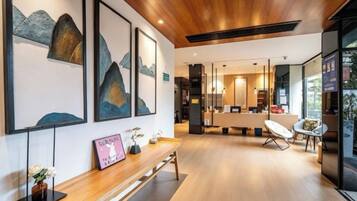 A modern interior with a wooden ceiling, a reception desk, framed artwork, and a seating area with a chair.