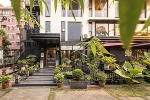 Un edificio con una escalera que lleva a la entrada, rodeado de plantas en macetas y un pequeño jardín.