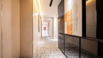 Pasillo de hotel con alfombra estampada, barandilla y un ascensor adosado a la pared.