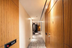 Un couloir d’hôtel aux murs en bois, au sol recouvert de moquette, et sur lequel est affiché un panneau indiquant le numéro de chambre 606.