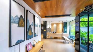 Ein modernes Interieur mit Holzbalkendecke, gerahmten Kunstwerken an der Wand, einer Bank und Blick ins Grüne durch eine Glasdoor.