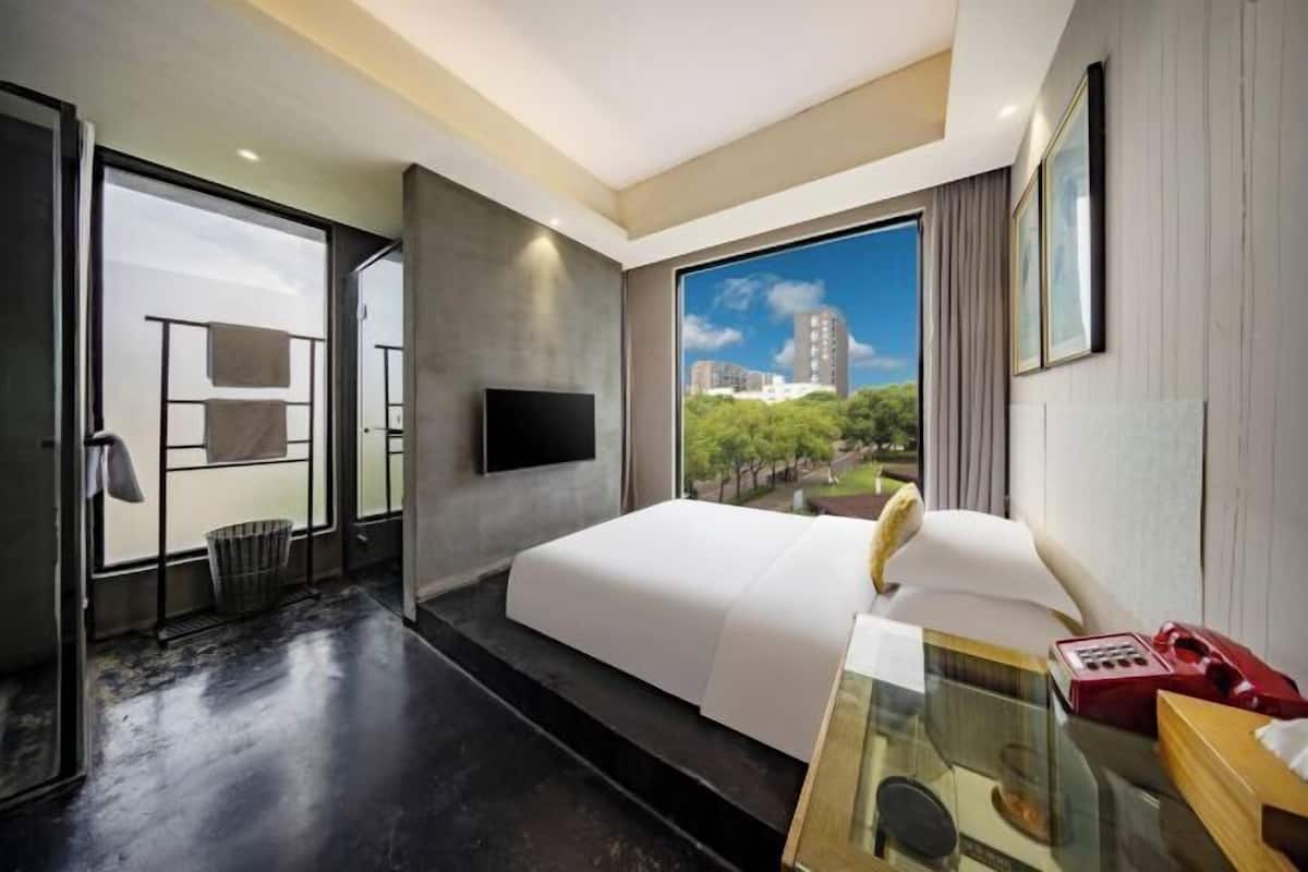 Una habitación de hotel moderna con una cama grande, televisor, una mesita de cristal y vistas a la ciudad.