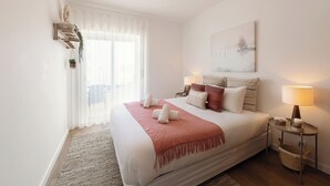 Une chambre à coucher bien aménagée, avec un grand lit, des lampes de chevet, une œuvre d’art accrochée au mur et une fenêtre ornée de rideaux légers.