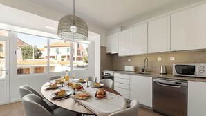 Une cuisine moderne avec des meubles blancs, un lave-vaisselle en acier inoxydable et une grande fenêtre donnant sur une cour.