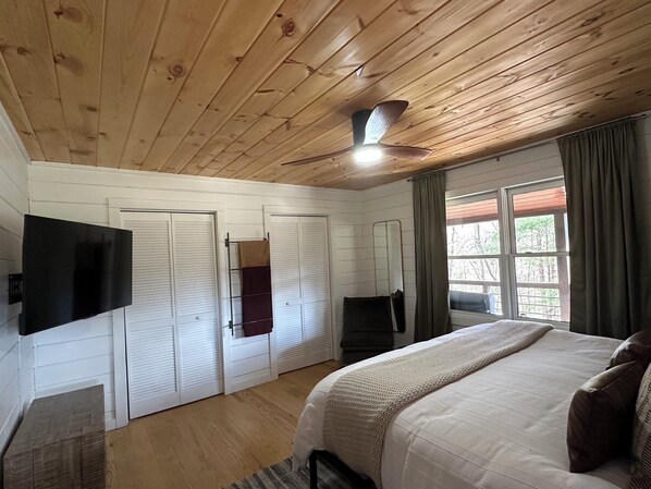 Une chambre avec un plafond en bois, un lit, une télévision, un ventilateur de plafond et une fenêtre avec des rideaux.