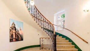 A grand staircase with ornate metal railings, a patterned floor, and a large painting of a cathedral. - Art Living Vienna (Vienna)