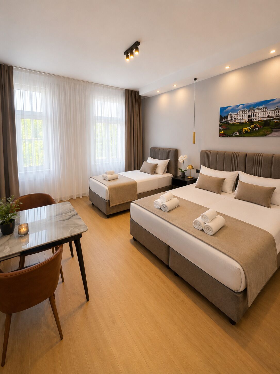 A hotel room with two beds, a dining table, and a painting on the wall.