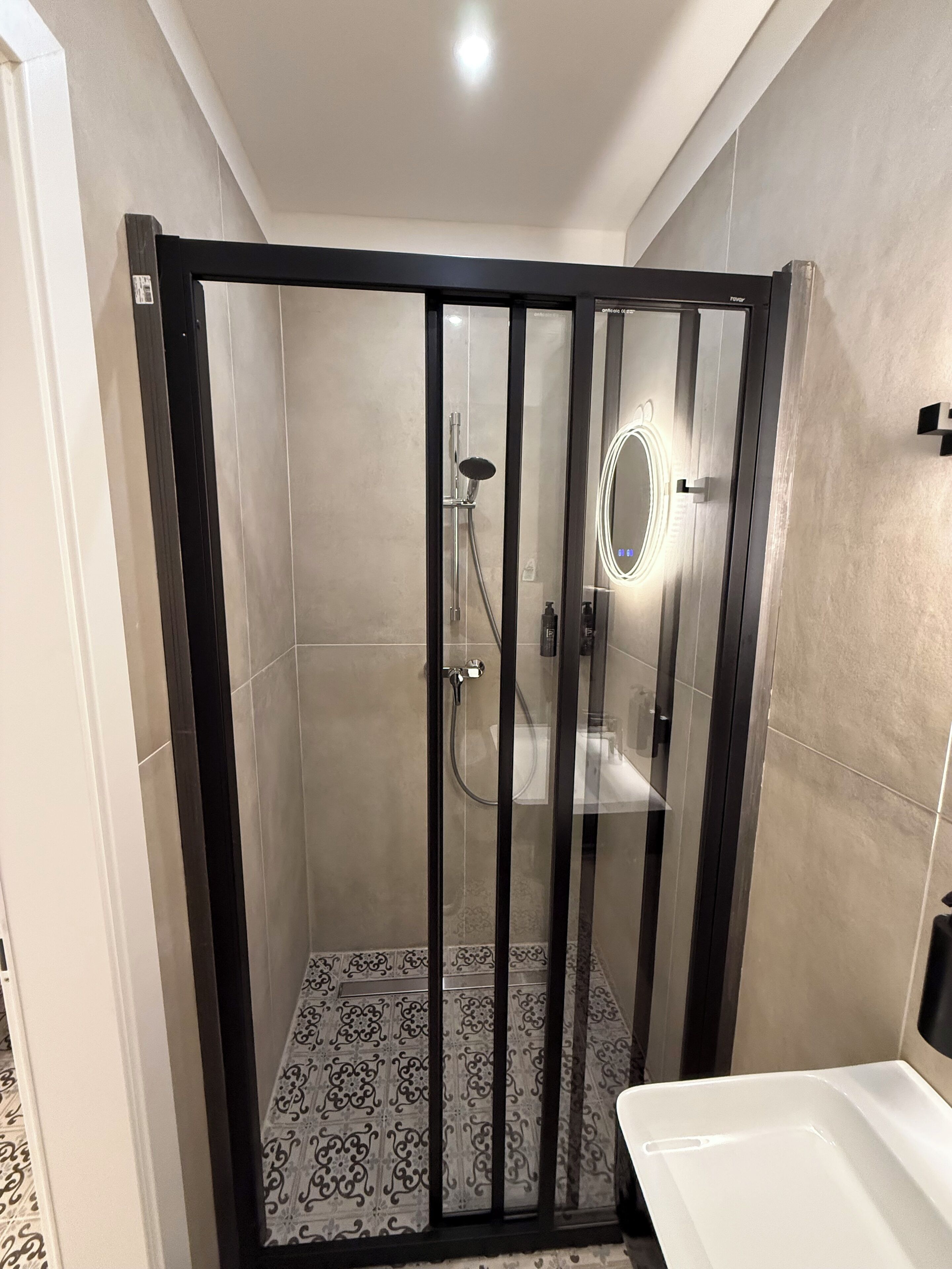Eine begehbare Dusche mit Glastür, ein Waschbecken und ein Spiegel mit Beleuchtung.
