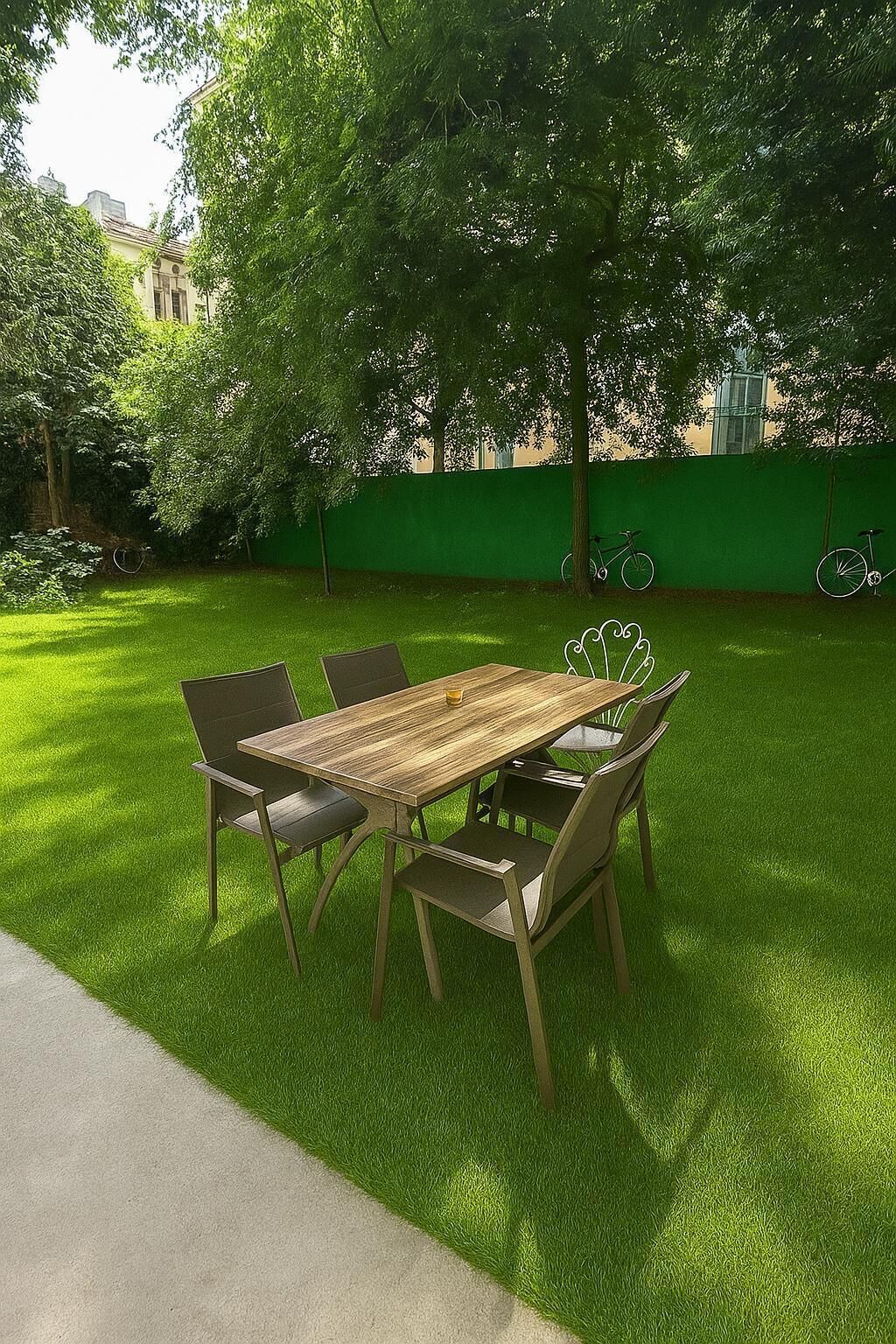A dining table with chairs in a grassy outdoor area, a bicycle, and a green wall in the background.