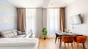 A modern hotel room with a bed, a desk, two chairs, a potted plant, and a TV on the wall. - Art Living Vienna (Vienna)