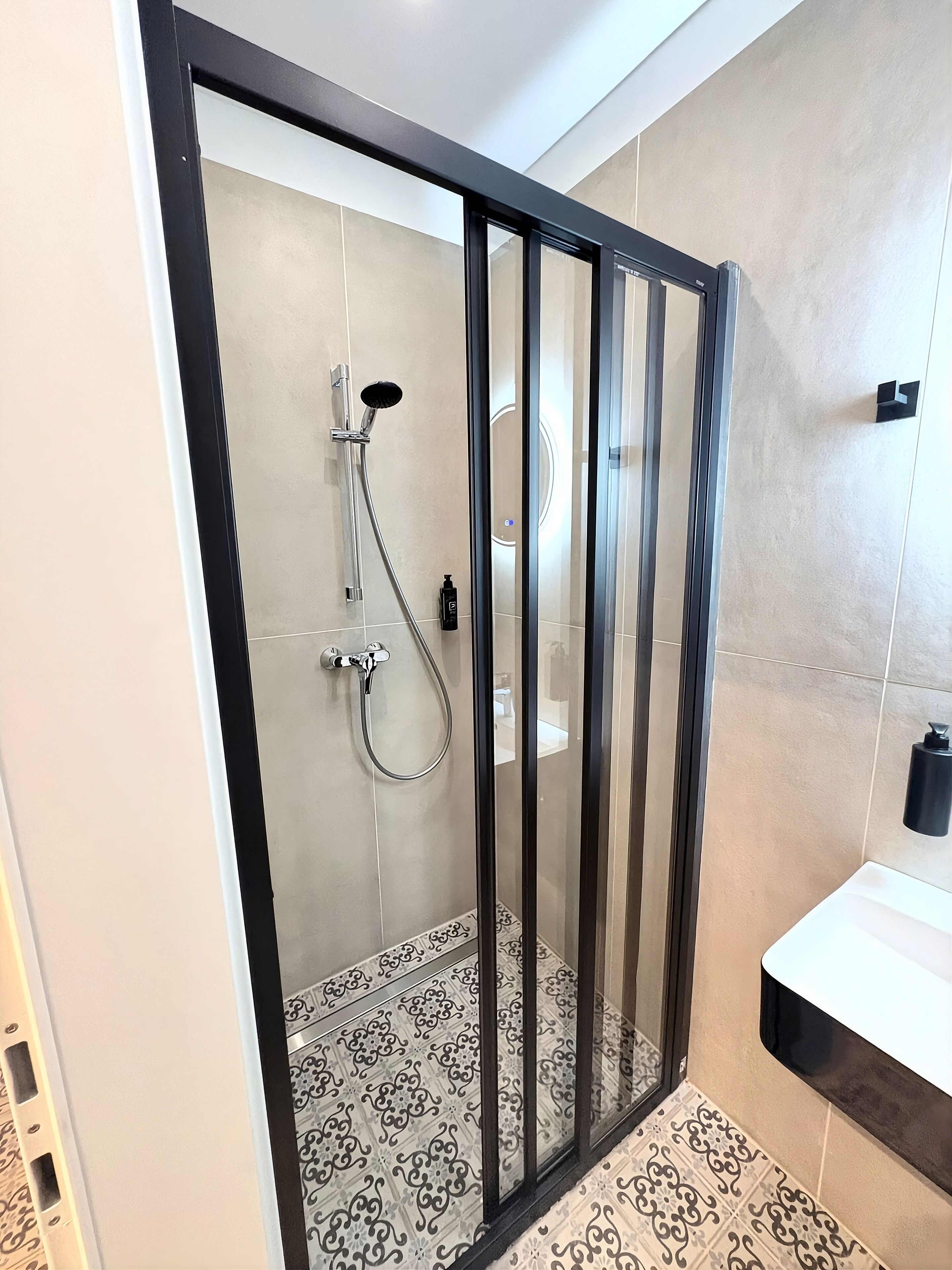 A modern bathroom with a glass-enclosed shower, a white sink, and patterned floor tiles.