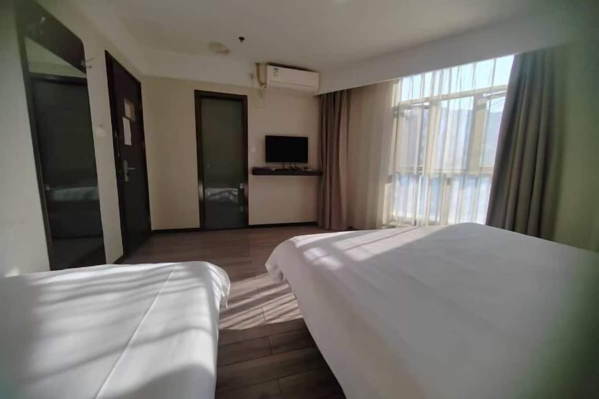 Habitación de hotel con dos camas, un televisor sobre un mueble, un equipo de aire acondicionado y un ventanal con cortinas.