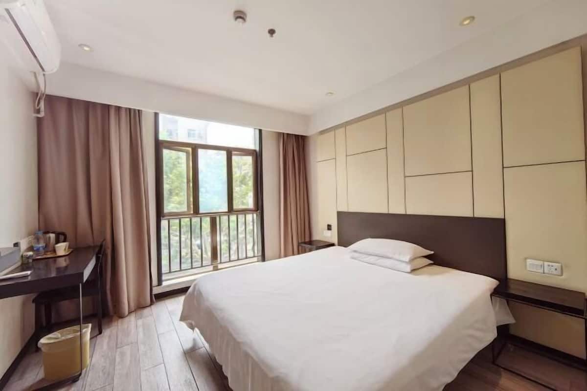 Una habitación de hotel con una cama grande, un escritorio, una silla y un ventanal con cortinas.