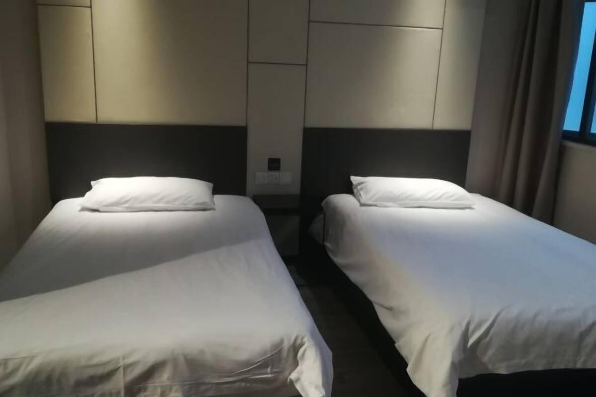 Habitación de hotel con dos camas individuales, cada una con colchón y almohada blancos, y un cabecero con interruptor de luz.