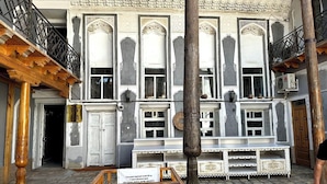 A traditional building with ornate architectural details, a wooden staircase, and a signboard in the foreground. - Shapira Boutique Hotel (Buxoro)