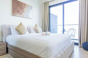 A modern bedroom with a large bed, a view of the city through the window, and a balcony with outdoor furniture.