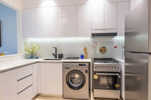 Eine moderne Küche mit weißen Schränken, einer Edelstahl-Waschmaschine, einem Daewoo-Gasherd und einem Kühlschrank.