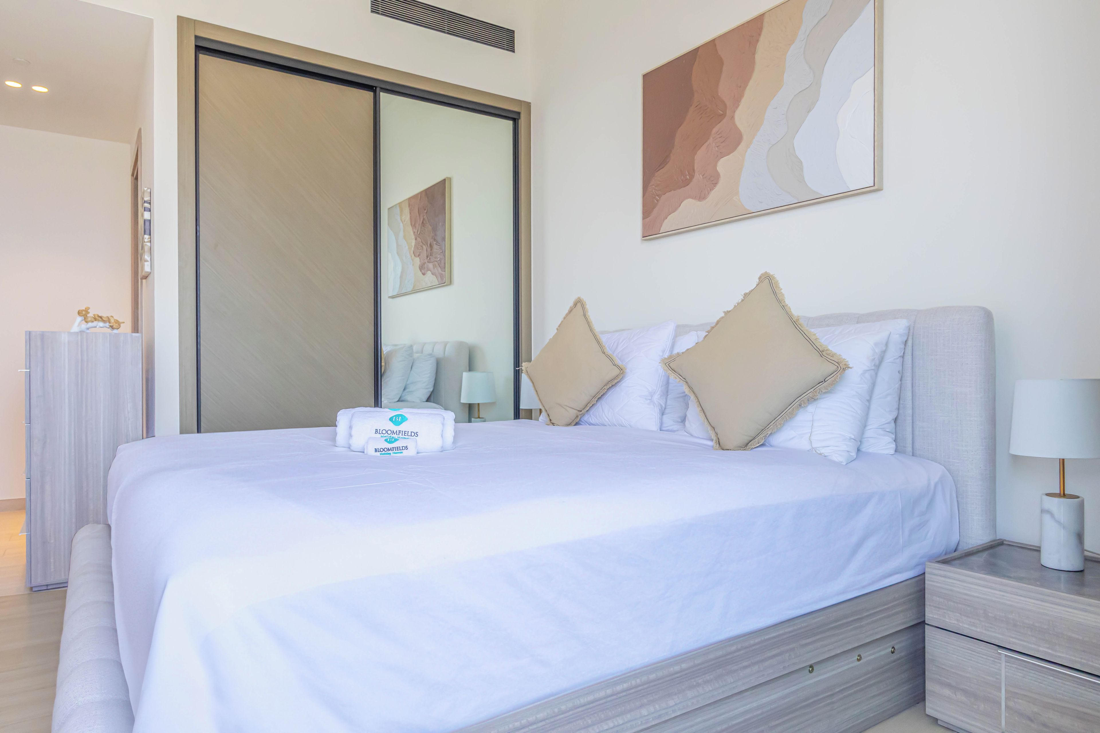 A hotel room with a large bed, a nightstand, a lamp, and a mirror.