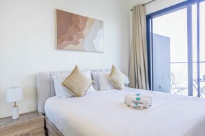 Ein Hotelzimmer mit einem großen Bett, zwei Kissen, einem Nachttisch mit Lampe, einem Fenster mit Vorhängen und einem Wandbild.