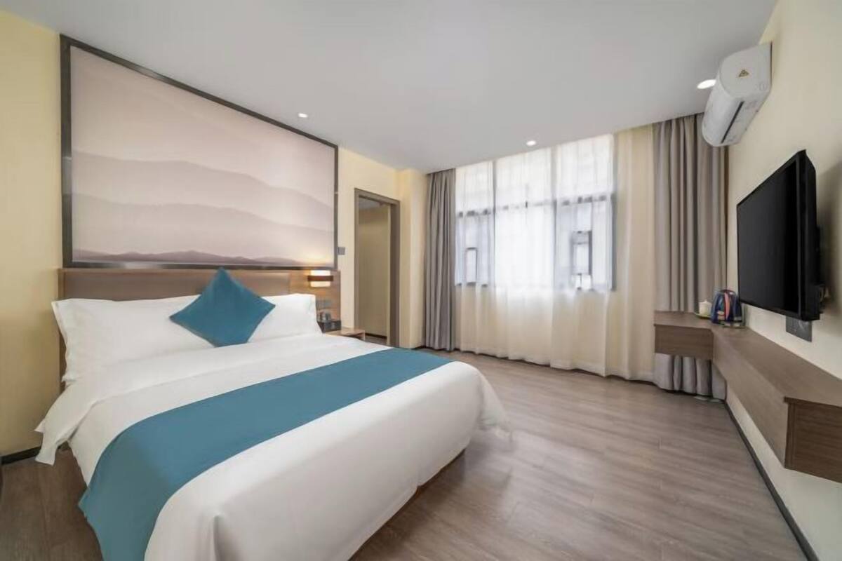 Habitación de hotel con una cama grande, un televisor de pantalla plana, una ventana con cortinas y un aire acondicionado de pared.