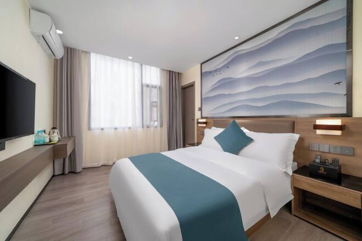 Habitación de hotel con una cama grande, un televisor de pantalla plana, un aire acondicionado instalado en la pared y un cuadro sobre la cama.