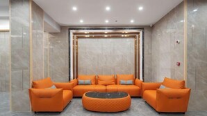 A lobby with a sectional sofa, ottoman, and marble walls. - Pomegranate Hotel (Guangzhou Baima Garment City Railway Station Subway Station Branch) (Guangzhou)