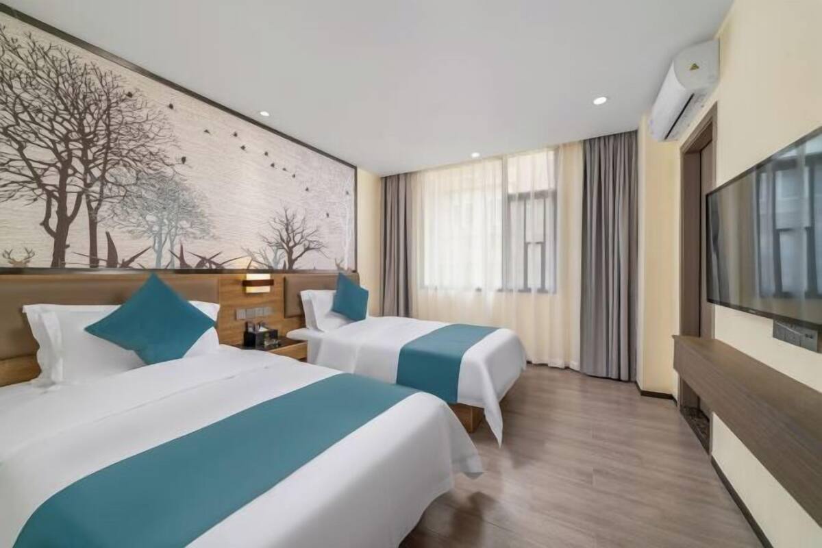 Habitación de hotel con dos camas, un mural grande en la pared, un televisor y una ventana con cortinas.