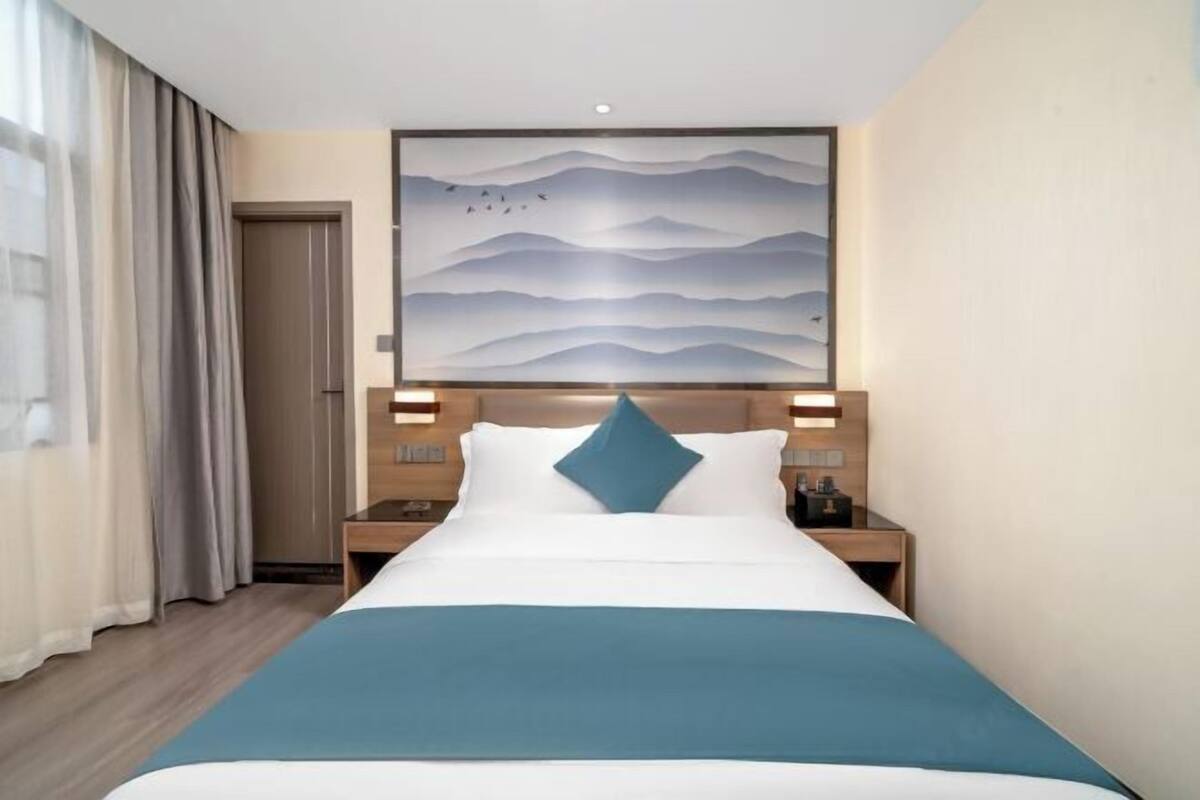 Una habitación de hotel con cama, mesita de noche, una obra de arte en la pared y una puerta.